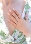 Mani con press on nails Brezza Floreale su abito floreale verde, mostrando sfumature naturali e fiori 3D realizzati con gel modellante artistico